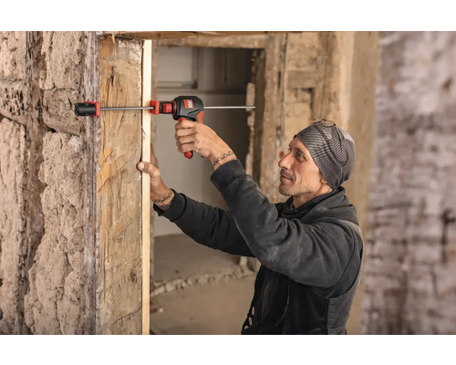 Mann befestigt eine Türzarge mit einem Spreizwerkzeug in einem renovierungsbedürftigen Raum.