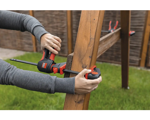 Eine Person befestigt mit einer Einhandzwinge zwei Holzstücke.