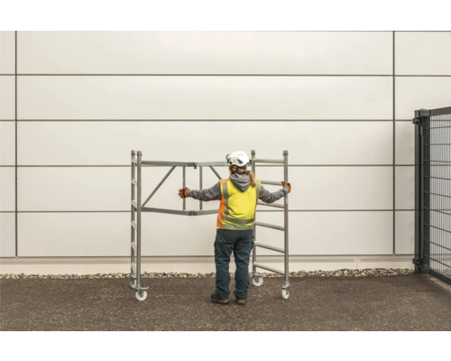 Un ouvrier du bâtiment pousse un échafaudage mobile.