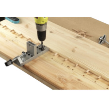 Eine Bohrmaschine bohrt Löcher in ein Holzbrett mit einem Dübelbohrgerät.