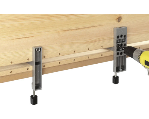 Une planche en bois est travaillée avec une perceuse et un gabarit de perçage