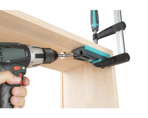 Une visseuse sans fil perce une planche en bois à l''aide d''un gabarit de perçage fixé par un serre-joint.