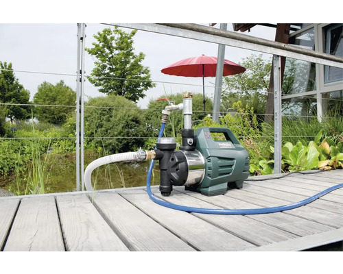 Station de pompage domestique Metabo avec tuyau flexible sur une terrasse en bois dans le jardin.