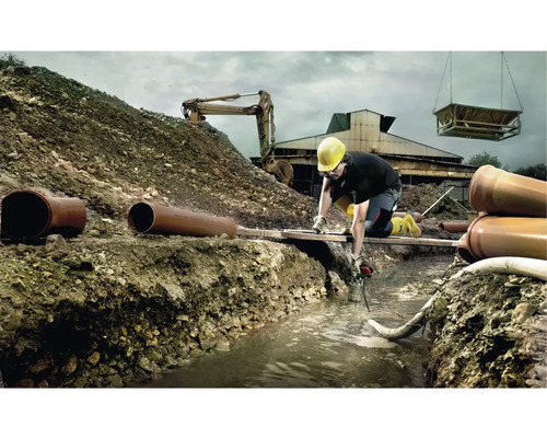 Ouvrier avec pompe submersible dans une tranchée, chantier avec excavatrice et tuyaux d''égout