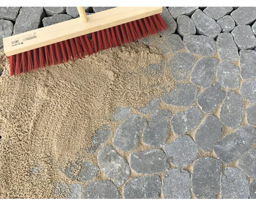 Les joints de pavés sont remplis avec un balai et du sable de jointoiement.