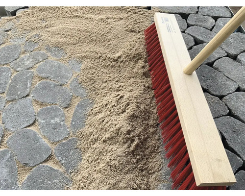 Scène avec des pavés, du sable de jointoiement et un balai de voirie