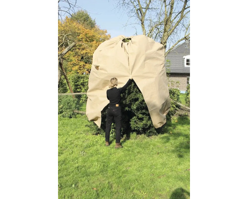 Une femme place une housse de protection sur un arbuste dans le jardin pour le protéger du froid.