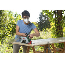 Frau mit Atemschutzmaske sägt Holzplatte mit Handkreissäge im Freien