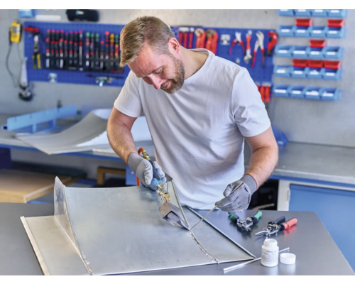 Handwerker beim Löten von Blechteilen in einer Werkstatt mit Werkzeugen und Werkbank