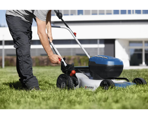 Une personne utilise une tondeuse à gazon sans fil sur une pelouse devant une maison.