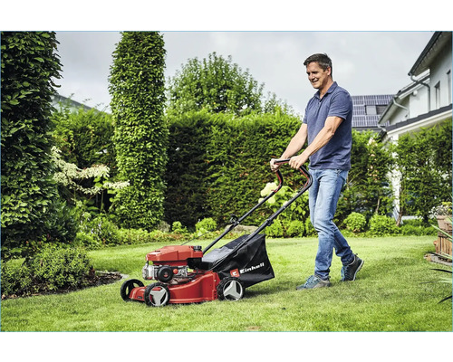 Un homme tond la pelouse avec une tondeuse Einhell dans le jardin.