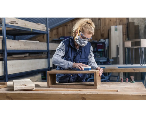 Femme ponçant une étagère en bois dans un atelier avec une cale à poncer