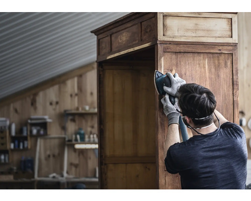 Mann schleift einen Holzschrank mit einem Schleifgerät.