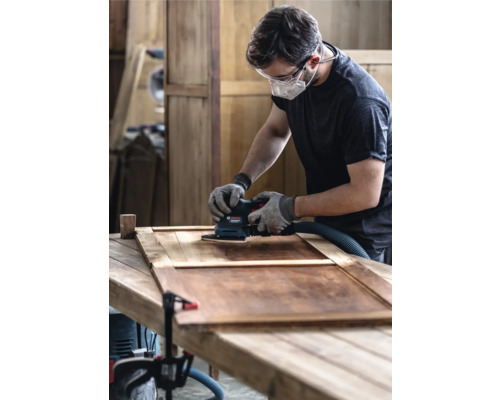 Homme ponçant une porte en bois avec une ponceuse vibrante