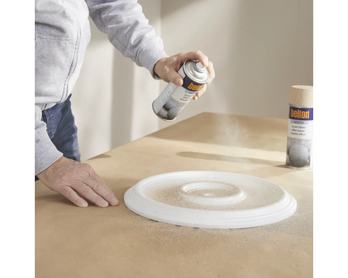 Une personne vaporise de la peinture sur une rosace avec un aérosol à effet granit