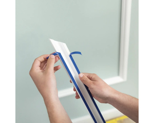 Une personne retire la bande de protection d''une moulure décorative.