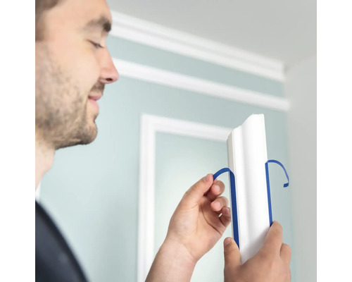 Un homme retire du ruban adhésif bleu d''une moulure décorative blanche.