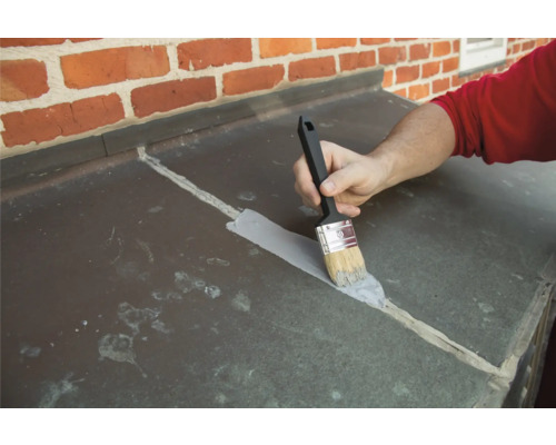 Eine Person trägt mit einem Pinsel eine Beschichtung auf ein Dach auf.