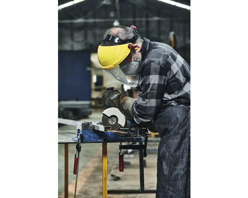 Handwerker mit Schutzvisier und Handschuhen schneidet Metall mit einer Schleifmaschine an einem Schraubstock.