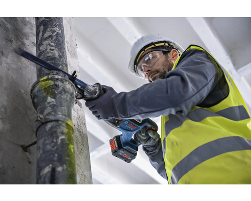 Un homme coupe un tuyau avec une scie sabre sans fil.