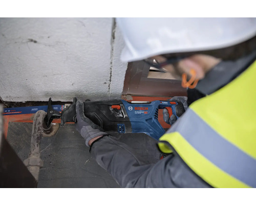Un homme avec un casque de protection scie un tuyau avec une scie sabre Bosch.