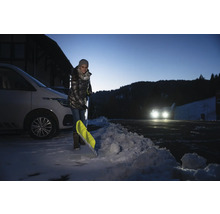 Frau schaufelt Schnee mit einer Schneeschaufel neben einem Auto.