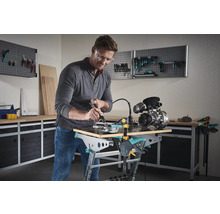 Un homme travaille avec un outil multifonction sur une pièce sur un établi. Des panneaux muraux à outils pour le rangement se trouvent à l''arrière-plan.