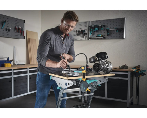 Ein Mann arbeitet mit einem Multifunktionswerkzeug an einem Werkstück auf einem Werktisch. Im Hintergrund befinden sich Werkzeugwände zur Aufbewahrung.