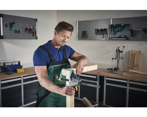 Un homme travaille avec une serre-joint à une main sur une pièce de bois dans un atelier.