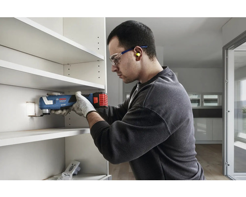 Un homme utilise un outil multifonction pour scier dans un compartiment d''étagère.