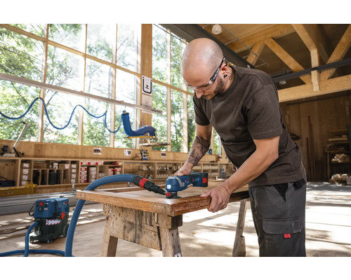 Artisan utilisant un outil multifonction pour travailler un cadre en bois dans un atelier.