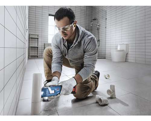 Un homme utilise un outil multifonction dans la salle de bains pour couper un tuyau.