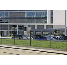Clôture à double fil devant un immeuble de bureaux et un parking.
