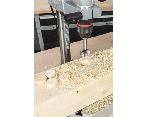 Standbohrmaschine beim Bohren eines Lochs in ein Holzbrett mit Holzspänen und Holzscheiben