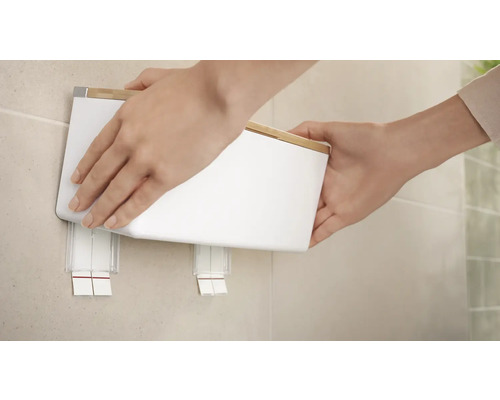 Hände befestigen einen weissen Wandbehälter mit Bambusdeckel an einer Wandhalterung.