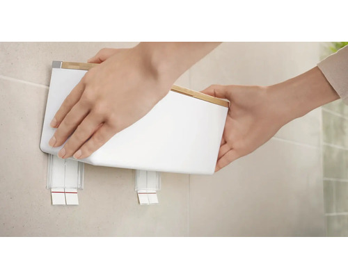 Person befestigt einen weissen Kosmetiktuchspender an der Wand