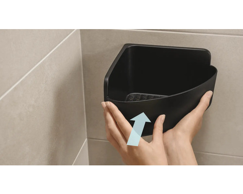 Une personne fixe une étagère d''angle noire dans la salle de bain.