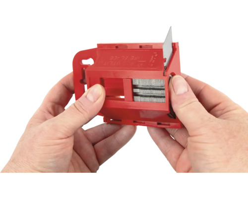 Les mains tiennent un changeur de lame rouge pour un cutter.