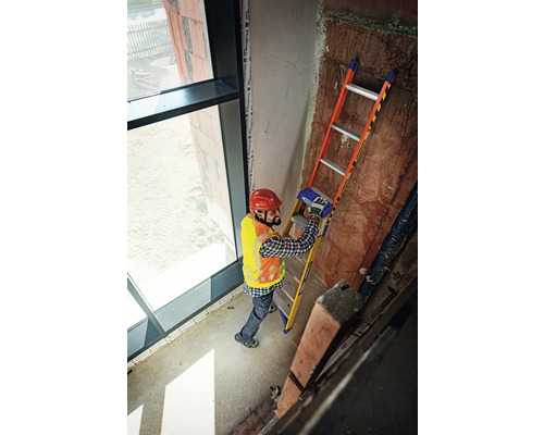 Un homme avec un casque et un gilet de sécurité se tient sur une échelle dans un bâtiment.