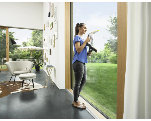 Une femme nettoie les fenêtres avec un aspirateur de vitres dans un salon lumineux.