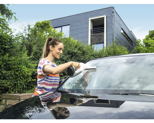 Une femme nettoie le pare-brise d''une voiture avec un aspirateur de vitres.