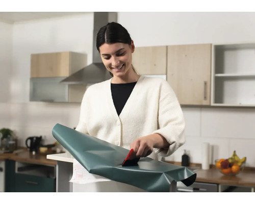 Femme appliquant un film adhésif avec une raclette dans une cuisine