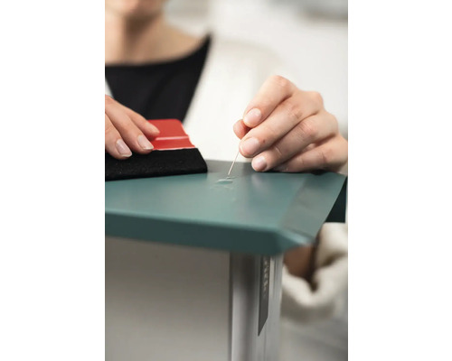 Une personne retire les bulles d''air d''un film à l''aide d''une aiguille et d''une raclette.