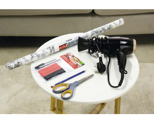 Film décoratif, racloir, cutter, sèche-cheveux, crayon et ciseaux sur une table