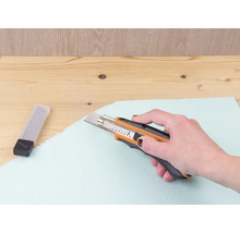 Une main coupe un panneau isolant avec un cutter.