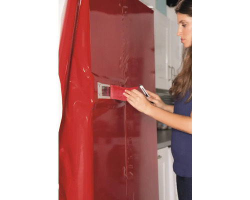 Frau bringt eine rote Möbelfolie an einem Kühlschrank mit einem Rakel und einem Messer an.