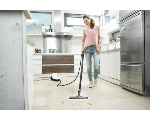 Frau reinigt Fliesenboden mit einem Dampfreiniger in einer Küche.