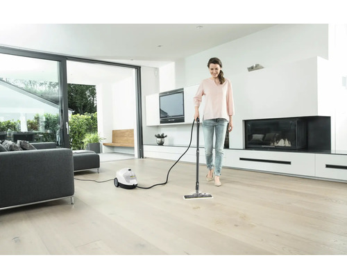 Femme nettoie parquet avec un nettoyeur à vapeur dans un salon lumineux.