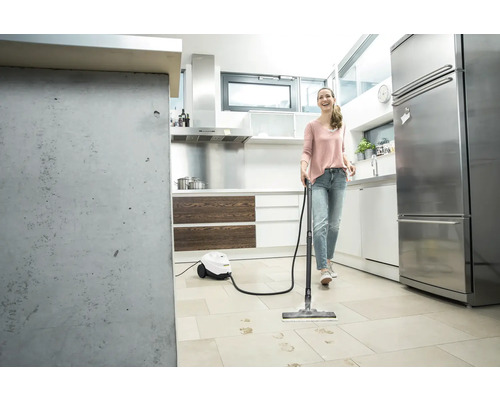 Femme nettoie un sol carrelé avec un nettoyeur vapeur dans une cuisine