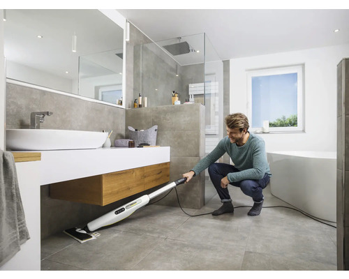 Un homme nettoie le sol d''une salle de bain avec un nettoyeur vapeur. La salle de bain comprend une douche, une baignoire et un lavabo.